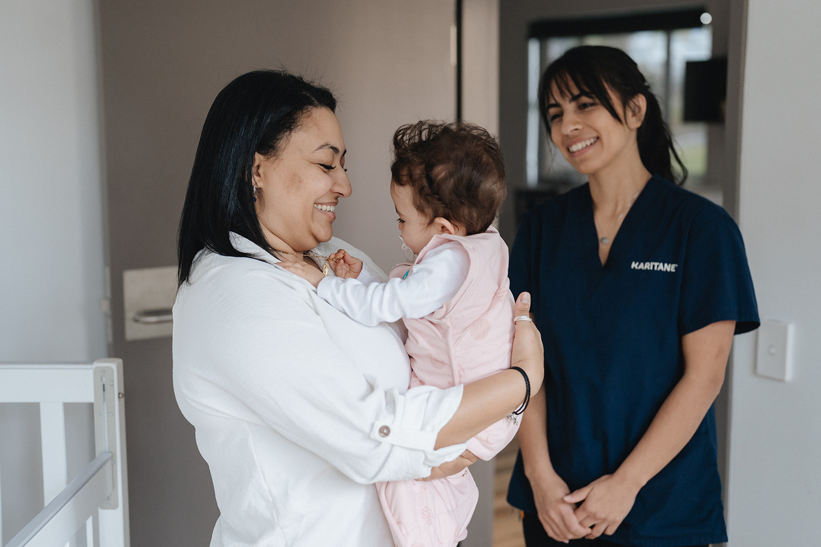 A smiling Karitane Nurse looking on as a mother holds her baby