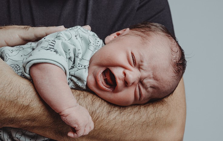 newborn on his father's arm screams crying with expression of suffering