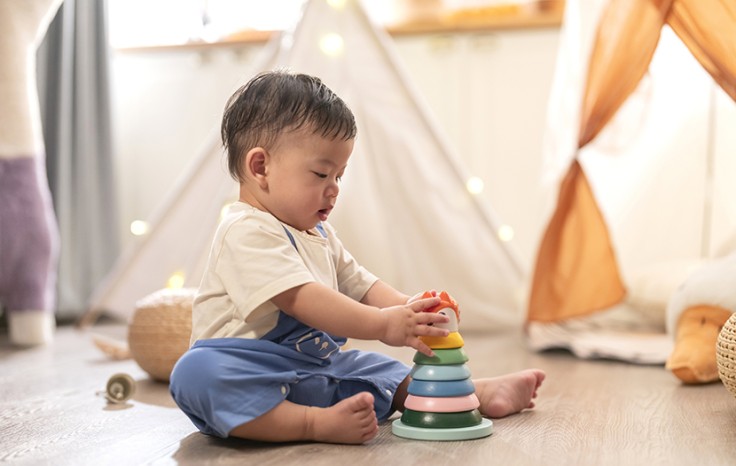 Happiness cutre asian boy 8-12 month playing sit relax and play wooden stack ring balance pratice hand muscle control smart colourful toy on carpet in living room at night home interior background