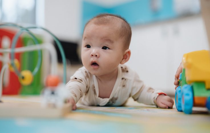 A baby having tummy time on the floor with toys